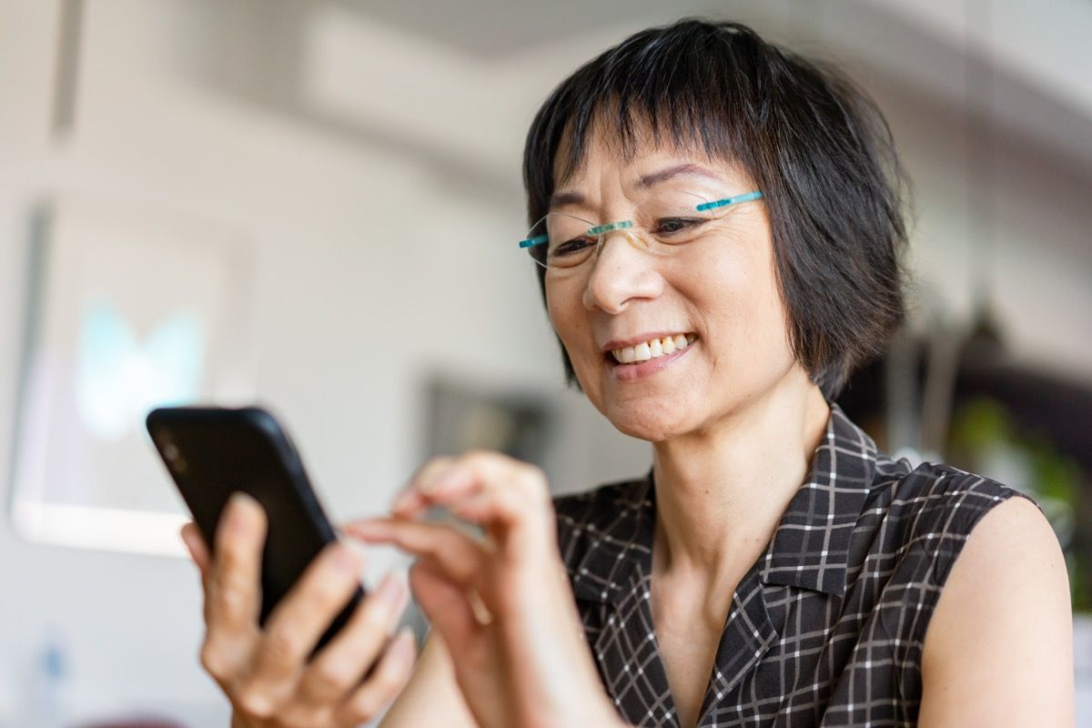Starší asijské žena se smíchem při používání smartphone.