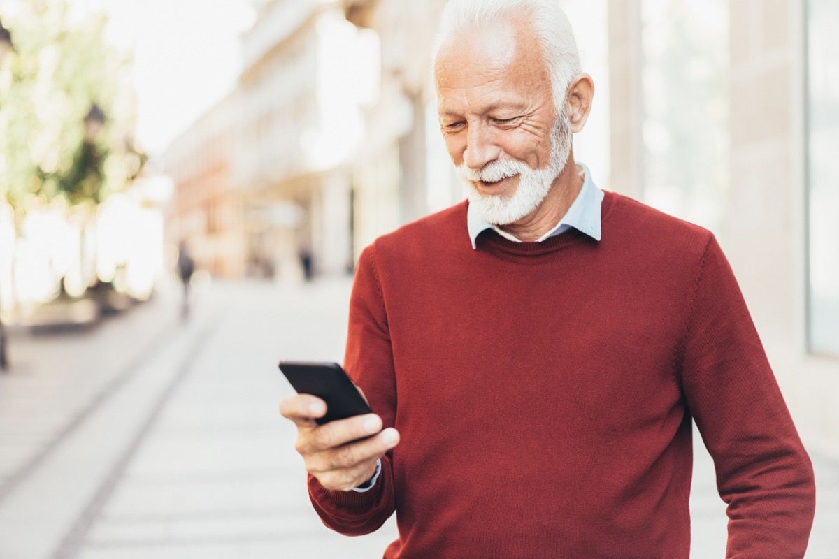 Умен непринуден старши мъж изпраща съобщения на открито на градската улица