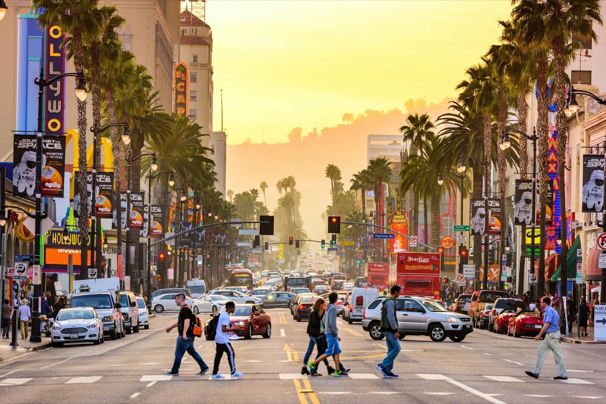 gājēji, ejot pāri ielai Holivudas bulvārī Losandželosā, Kalifornijā krēslas stundā