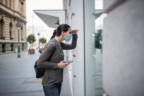   Žena v ochrannej maske používa mobilný telefón. Je vonku, na ulici. Belehrad, Srbsko