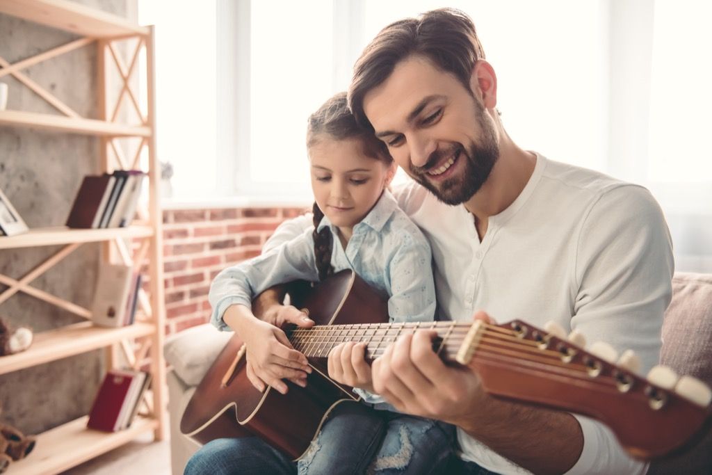 איש מחזיק ילדה צעירה, מלמד אותה לנגן בגיטרה