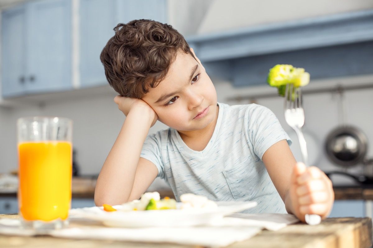 Băiat tânăr care se uită la broccoli care mănâncă la cină