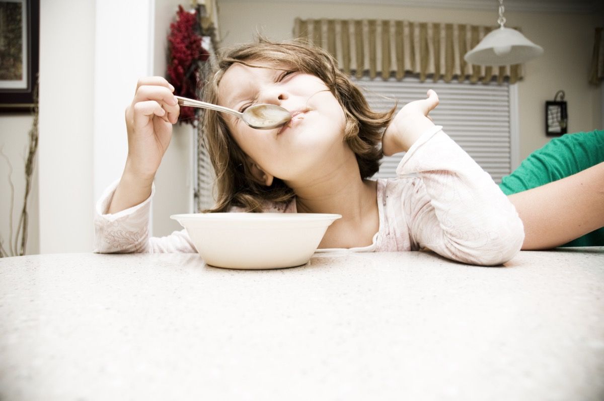 Fiatal lány eszik gabonaféléket a könyökével az asztalon, hogy pimasz