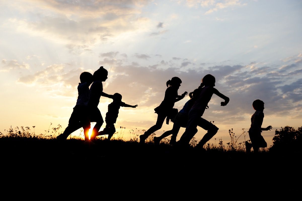 सूर्यास्त के समय एक मैदान में दौड़ते बच्चे