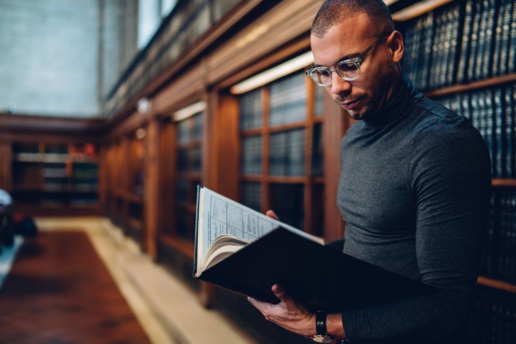 Taitava ammattilaisjuristi viettää aikaa lakien oppimiseen julkisessa kirjastossa, keskittynyt mies toimittaja lukee tietokirjoja analysoi tietoja seisova uutishylly