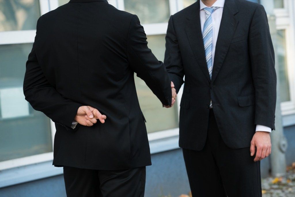 Keskiosa epärehellistä liikemiestä sormin ristissä kättelemällä kumppanin kanssa ulkona