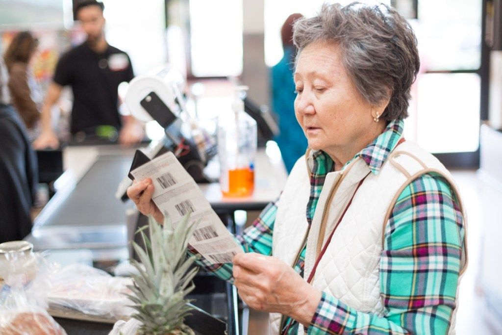 Preudarna starejša ženska si ogleduje kupone, preden plača za živila.