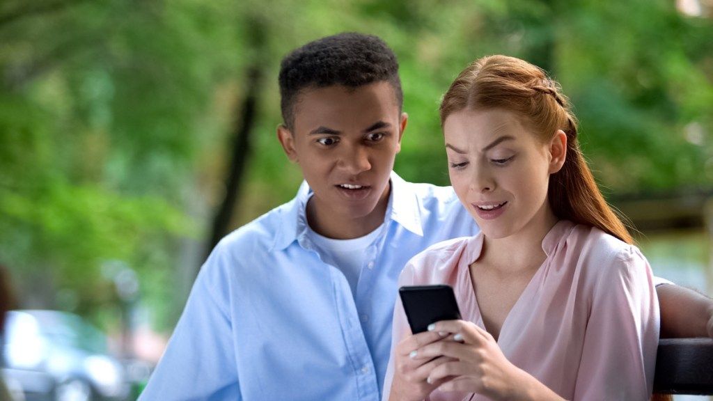 Шокирана тийнейджърска двойка от смесена раса, гледаща снимки от социалната мрежа през телефона