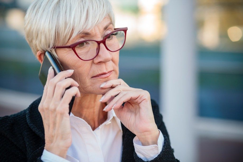 นักธุรกิจหญิงที่เป็นผู้ใหญ่ขี้กังวลกำลังคุยโทรศัพท์มือถือวางแขนไว้ที่คาง แนวคิดทำงานได้ทุกที่