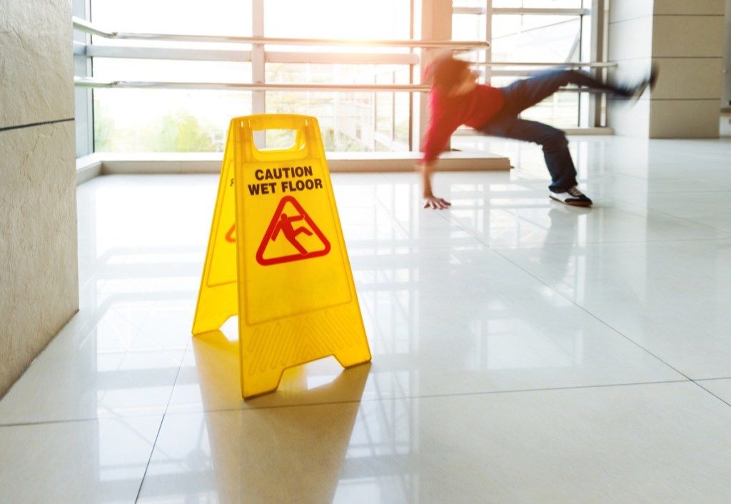 Žmogus nuslysta ant drėgnų grindų šalia drėgnų grindų atsargumo ženklo.