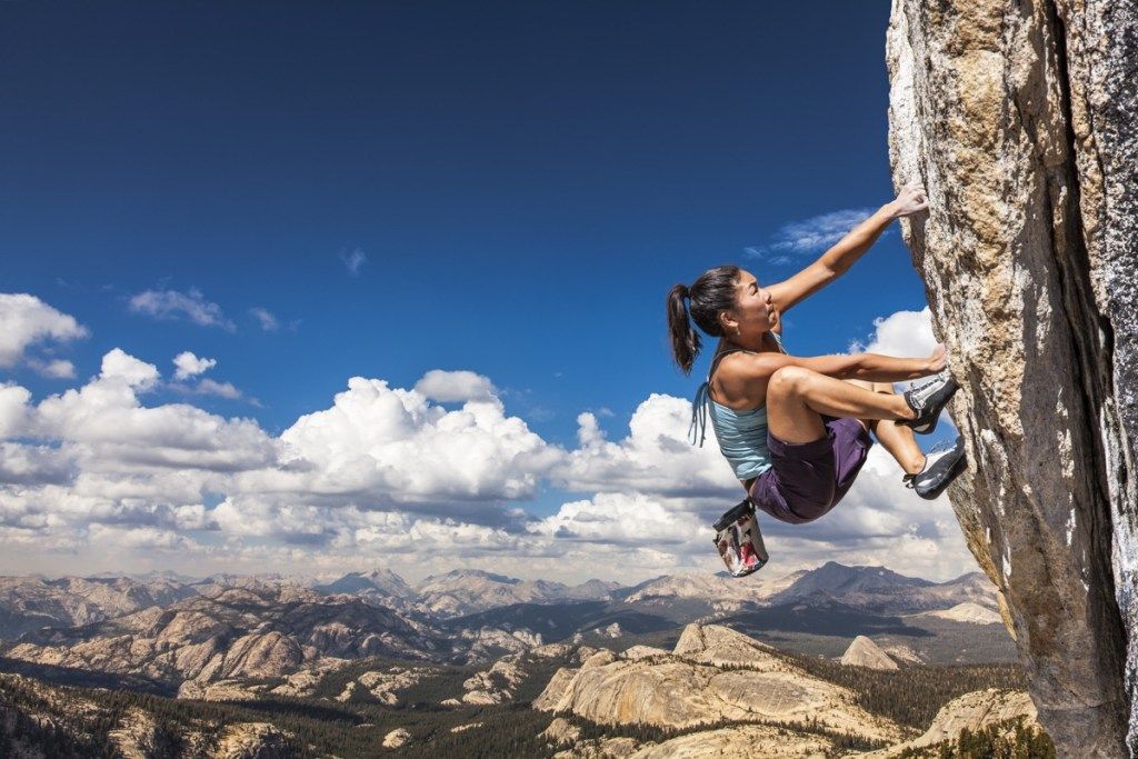 Sievietes alpīniste šūpojas no izaicinošas klints malas.
