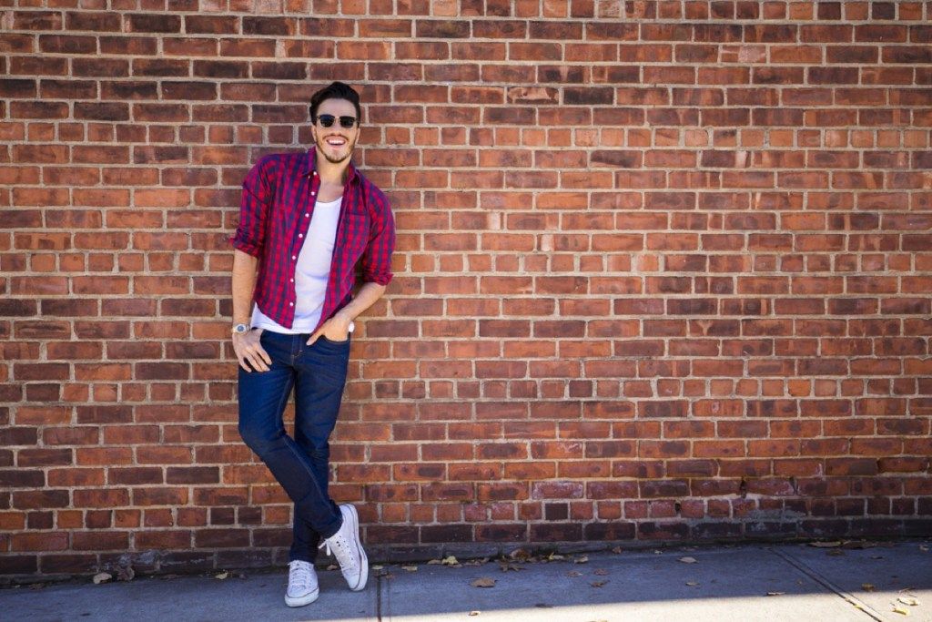 vyras su liesais džinsais, stovintis prie plytų sienos