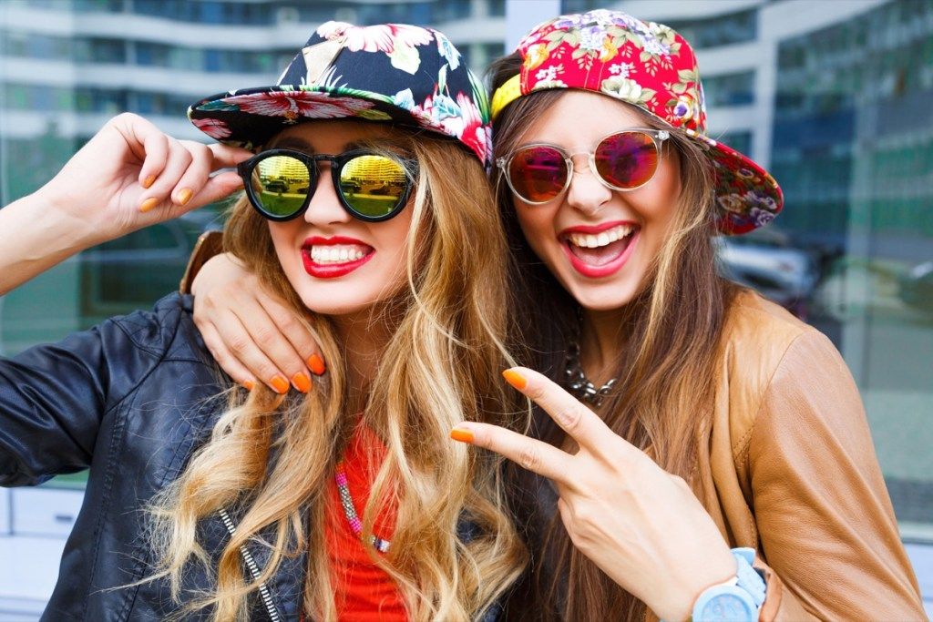 Dvi moterys, dėvinčios gėlėtas tiesaus kepurės kepures su akiniais nuo saulės