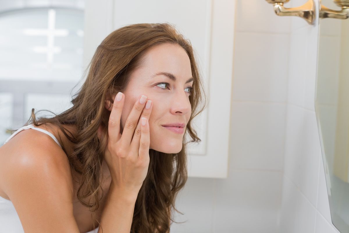 Šoninis moters vonios kambario veidrodyje veidą nagrinėjančios moters vaizdas