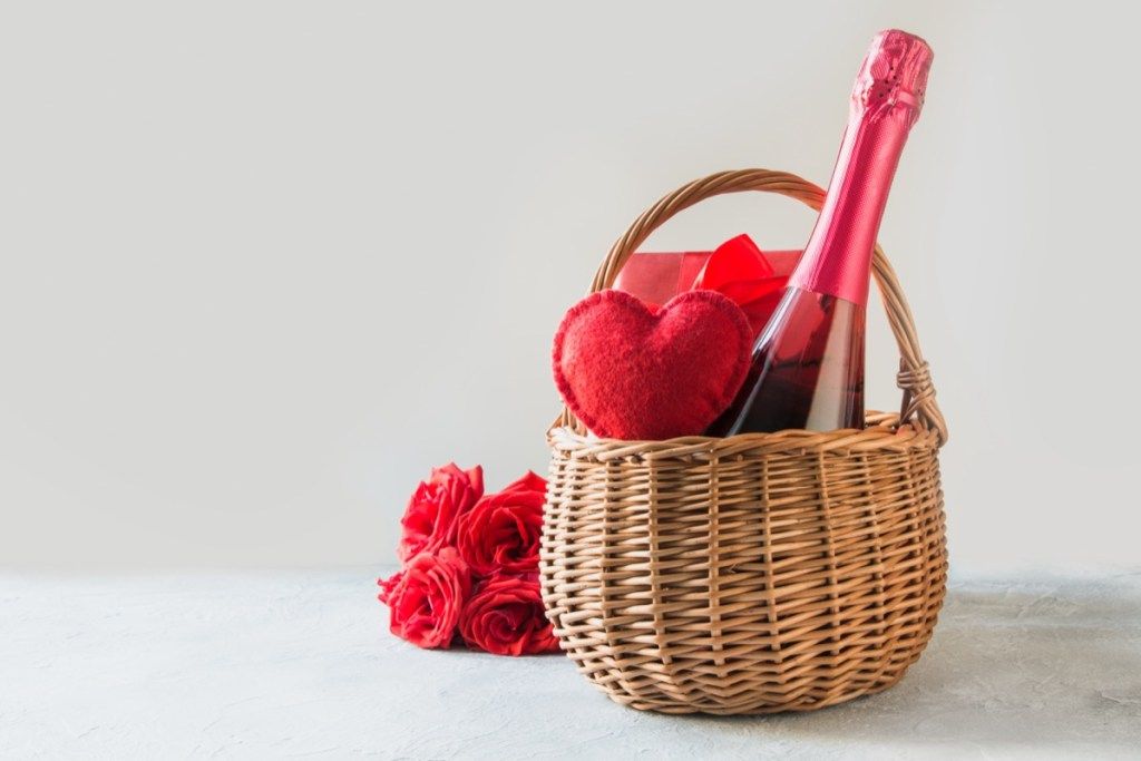 steklenica šampanjca in rdečega srčka v košarici ob šopku rož
