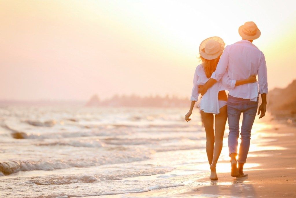 par u šeširima šetajući plažom u zalasku sunca - novac može