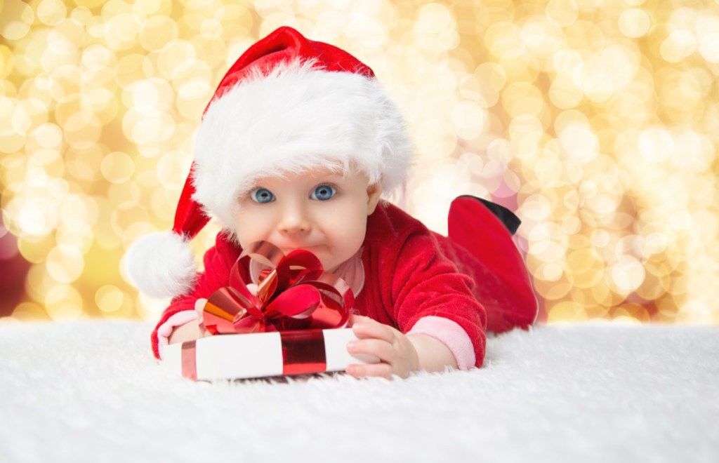 dojenček v božičnem onesieju, ki ima darilo