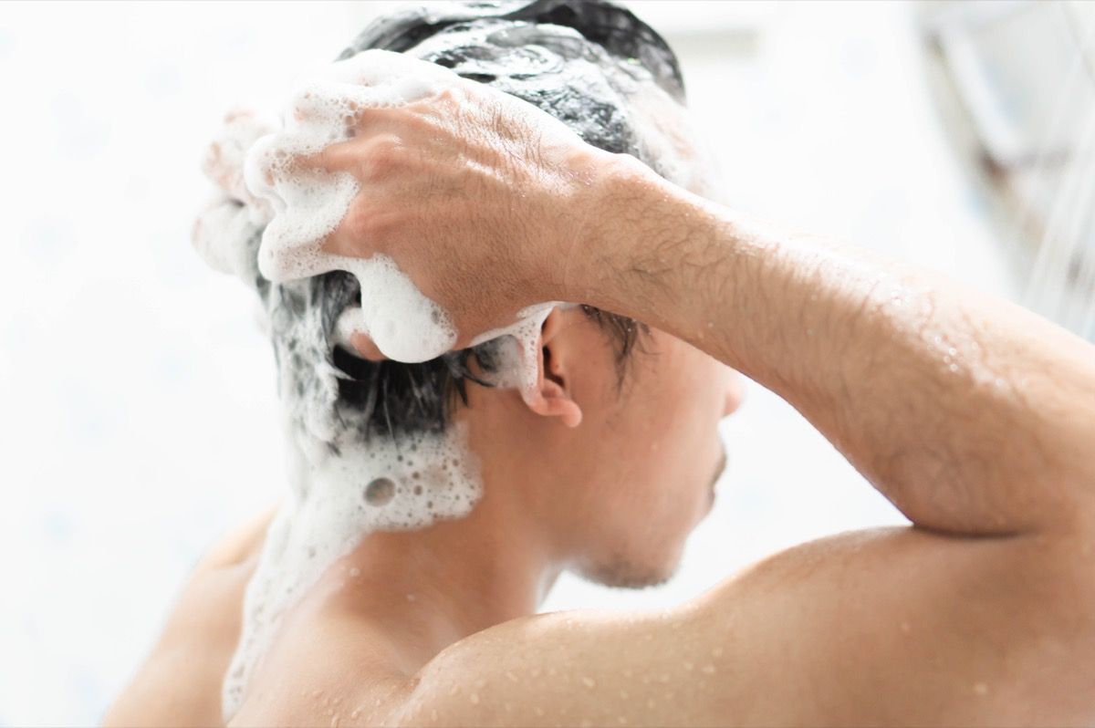Cilvēks mazgā matus ar šampūnu dušā