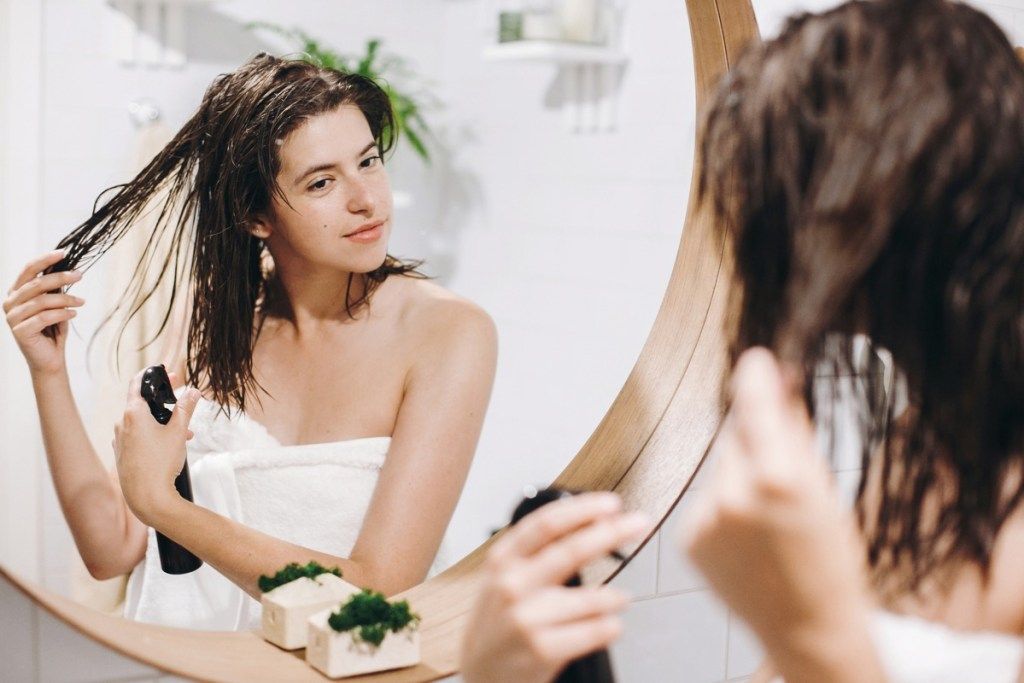 Sieviete, ievietojot produktu matos pie vannas istabas spoguļa