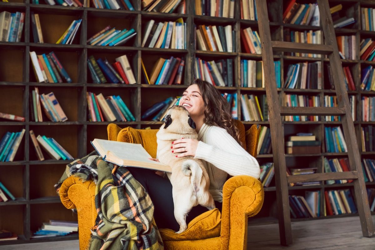 Tyttö lukee kotikirjastossa koiran kanssa