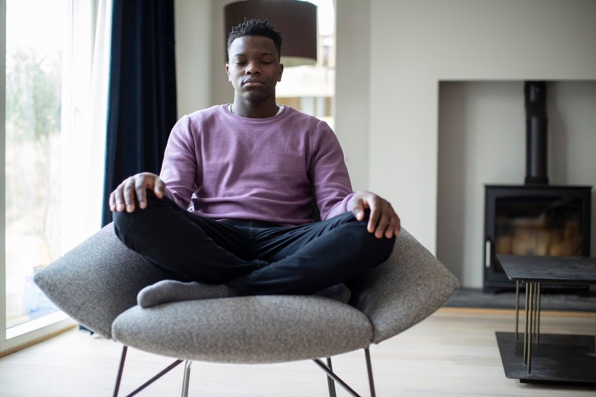jauns, melns vīrietis meditē krēslā