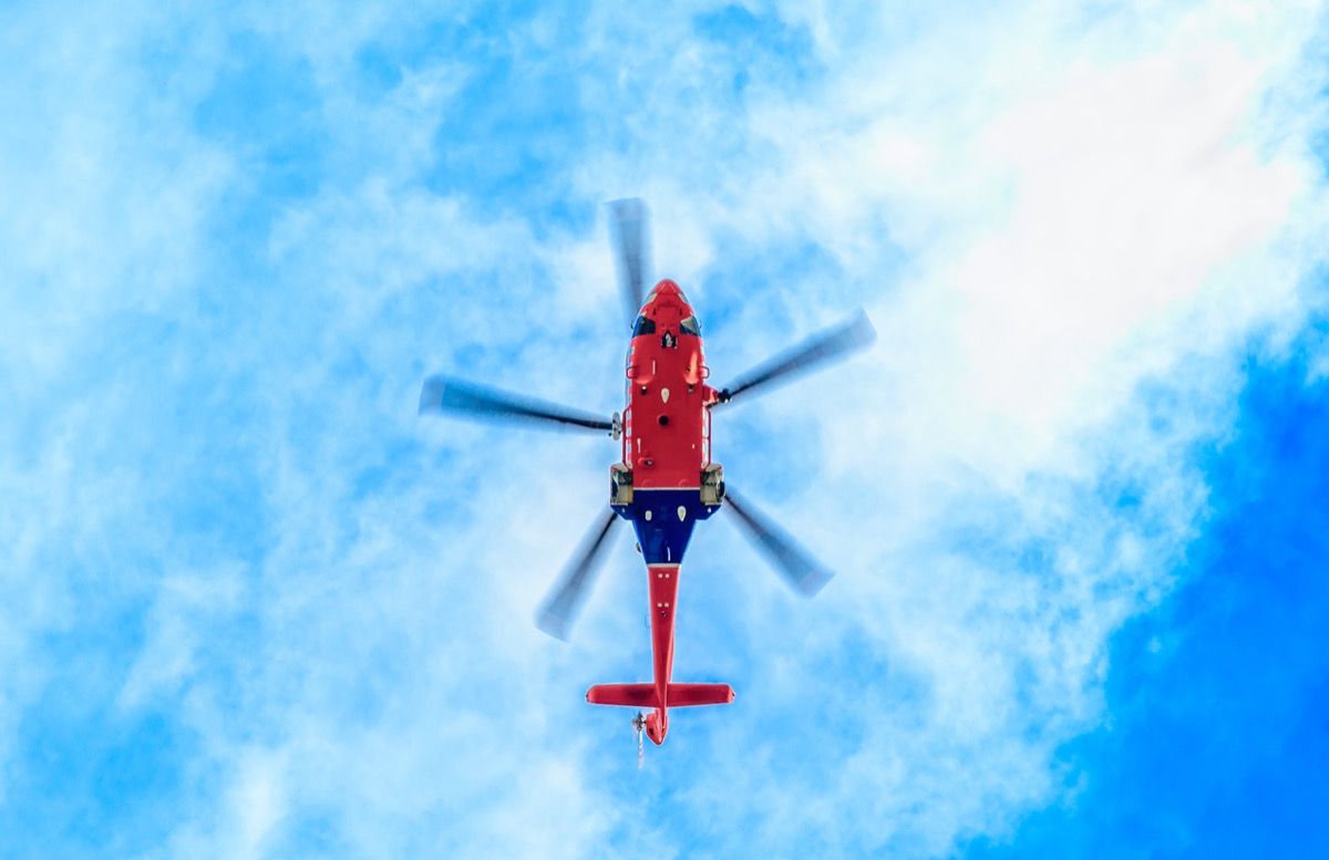 гледайки отдолу синьо-червен хеликоптер срещу синьо небе със светли облаци