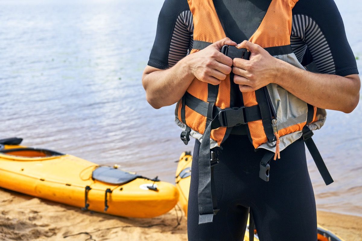 Человек соединяет свой спасательный жилет перед озером