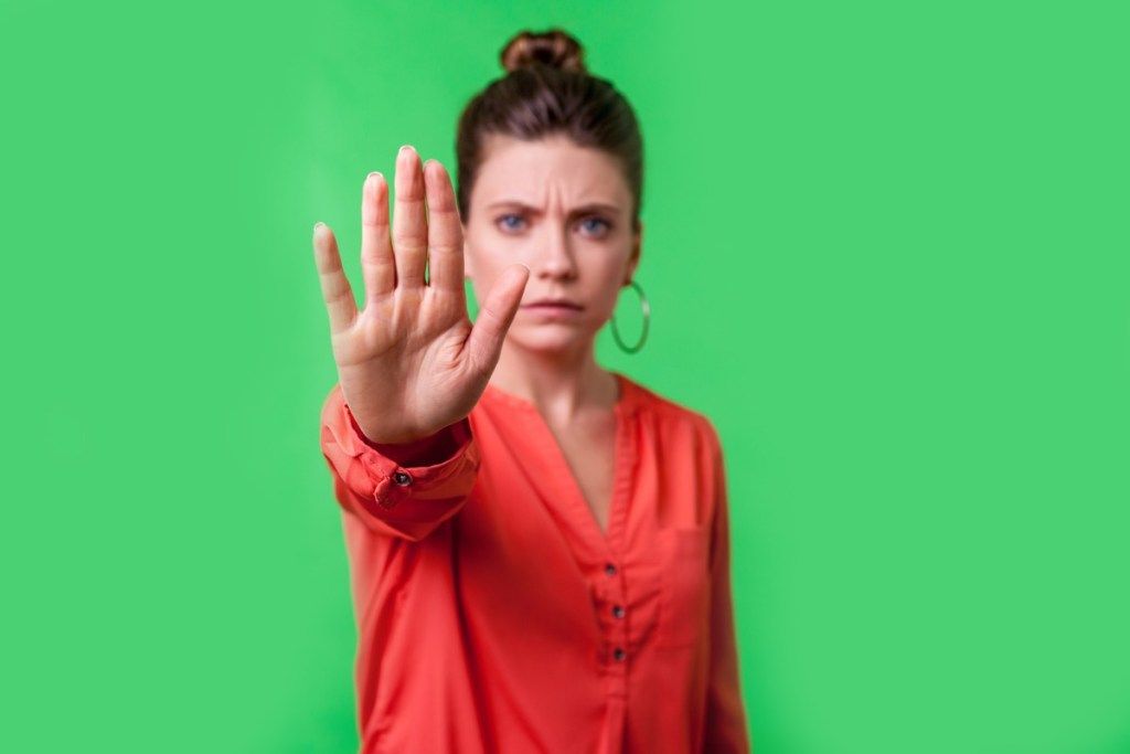 Nehaj, ne! Portret jezne ali zaskrbljene mlade ženske s pričesko s pecivom, velikimi uhani in v rdeči bluzi, ki se namrščeno preganja s kamero, prepoved. notranji studijski posnetek, izoliran na zelenem ozadju (Stop, ne! Portret jezne ali zaskrbljene mlade ženske