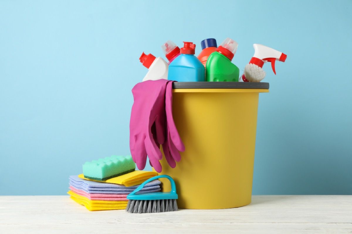 Suministros de limpieza coloridos en balde amarillo sobre fondo azul.