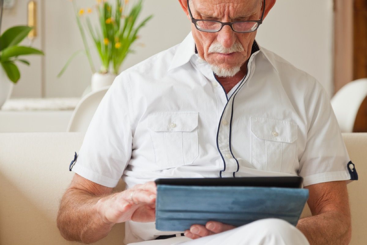 người đàn ông da trắng lớn tuổi sử dụng máy tính bảng của mình trên đi văng