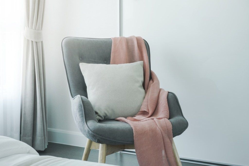 szürke kárpitozott szék rózsaszín takaróval és fehér párnával