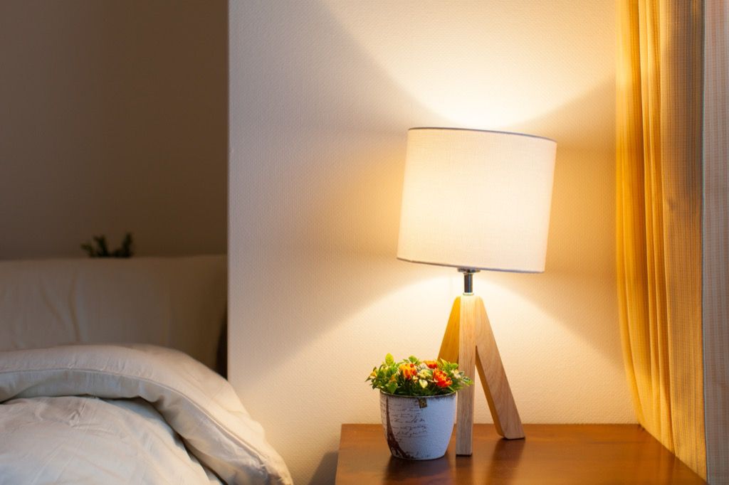 白いベッドの横にある木製のナイトスタンドに三脚木製ランプ