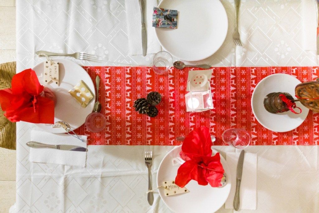 jedálenský stôl s bielymi taniermi a červeným sviatočným behúňom