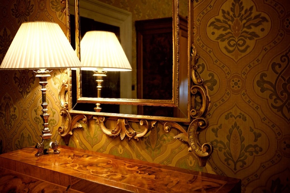 vecmodīgs lampa priekšā apzeltīts spogulis uz kredenza
