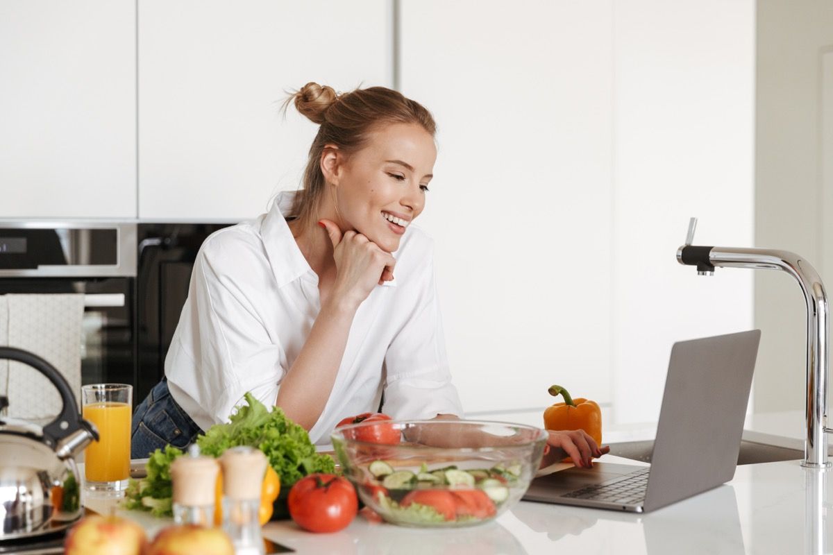 Žena koja kuha u kuhinji sa svojim prijenosnim računalom