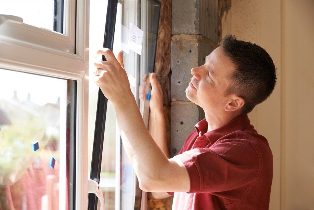 mees paigaldab energiasäästlikke aknaid kliendiarve vähendamiseks