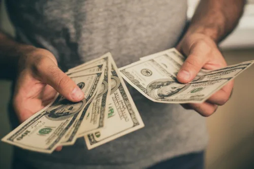   En mann i en grå t-skjorte holder dollar i hendene. Bank. Kasino. Lønn. Priser.