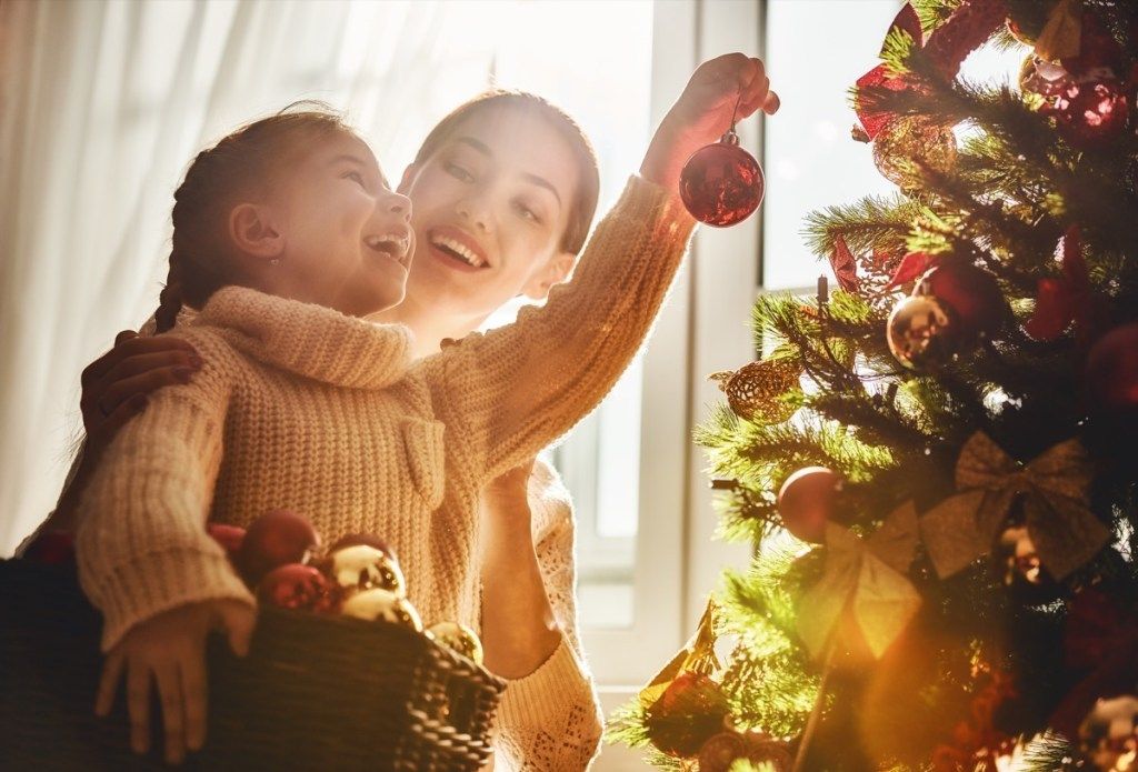 माँ और बेटी एक क्रिसमस पेड़ पर गहने लटकाते हैं