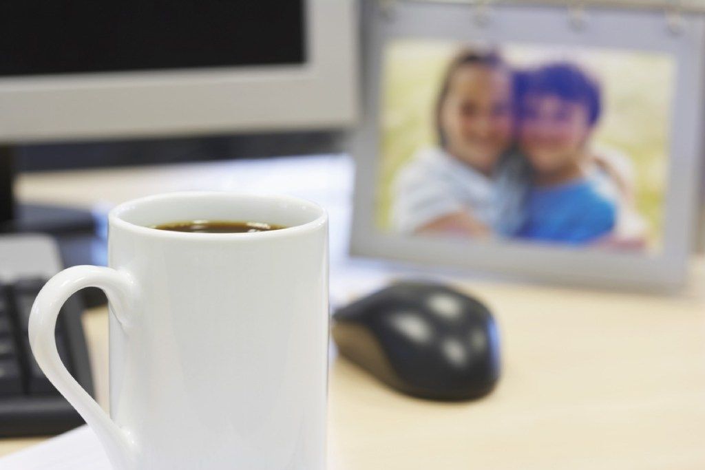 stalas su pele, kavos puodelis ir šeimos nuotrauka, biuro etiketas