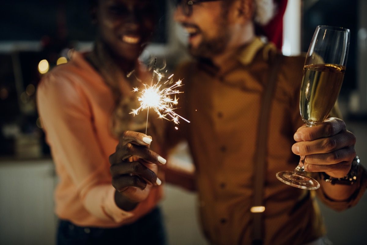 नए साल पर स्पार्कलर और शैंपेन ग्लास पकड़े हुए आदमी और औरत