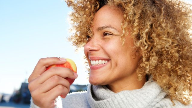  Страничен портрет отблизо на здрава млада афро-американка, която държи ябълка