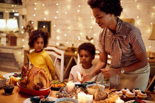   אמא אפרו אמריקאית מדליקה נרות במהלך ארוחת חג ההודיה ליד שולחן האוכל.