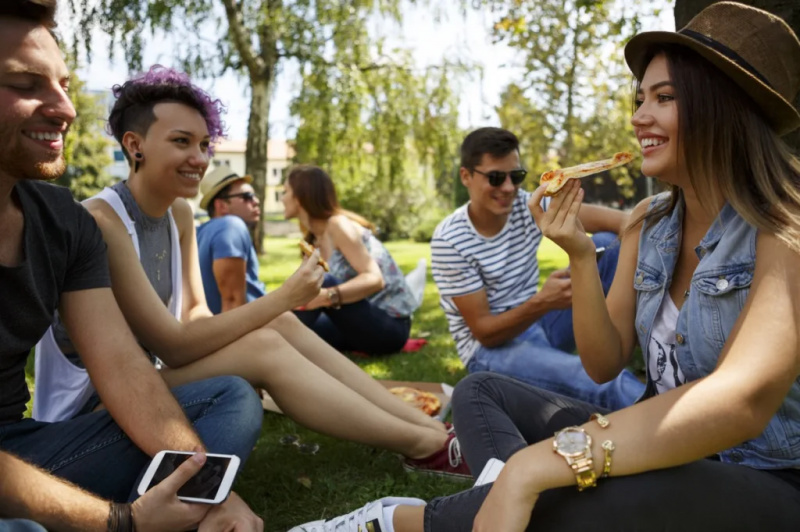   ľudia sa zhromažďujú v parku, jedia pizzu, žiadne masky