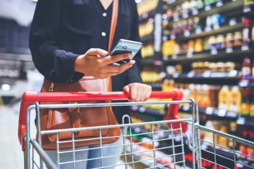   Rajattu kuva naisesta, joka käyttää älypuhelinta tehdessään ostoksia ruokakaupassa
