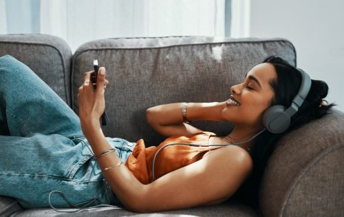   Snimka mlade žene koja koristi pametni telefon i slušalice na sofi kod kuće