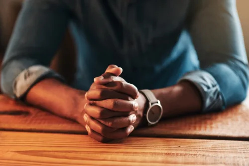   Przycięte zdjęcie nierozpoznawalnego biznesmena siedzącego z rękami w swoim domowym biurze i modlącego się