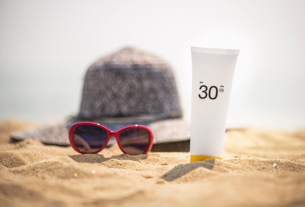 sončna očala in zaščitna krema SPF, ki sedijo na plaži, zdrava koža po 40 spf