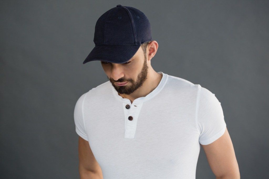Hombre vestido con una camiseta henley de manga corta blanca y una gorra azul marino