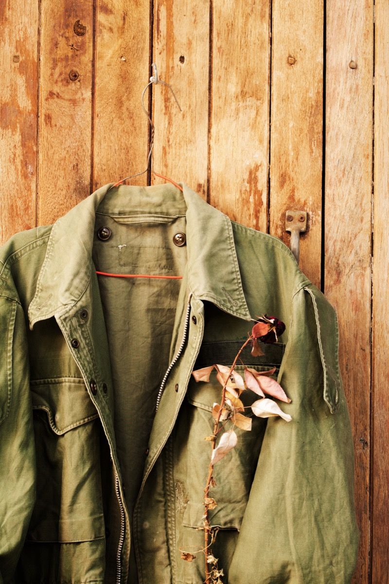 Zelená vojenská poľná bunda so suchou ružou vo vrecku zavesená na drevenom paneli - Obrázok