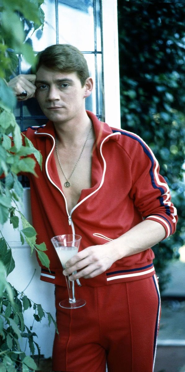 Anthony Andrews na svojem vrtu v angleškem Wimbledonu, oblečen v rdečo trenirko, modna osemdesetih